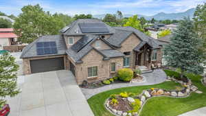 View of front of home with solar panels, driveway, roof with shingles, a front yard, and brick siding