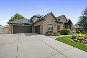 View of front of property with an attached garage, a gate, driveway, roof mounted solar panels, and brick siding