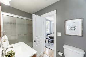 Full bath featuring vanity, toilet, wood finished floors, a textured ceiling, and a shower with door