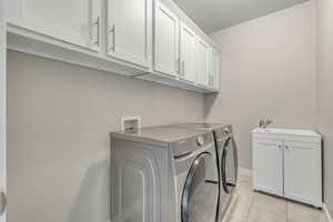 Washroom featuring cabinet space, washer and clothes dryer, light tile patterned floors, and baseboards