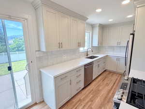 Kitchen with appliances with stainless steel finishes, a sink, light wood-style floors, tasteful backsplash, and light stone counters
