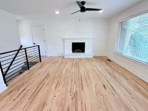 Unfurnished living room featuring a ceiling fan, wood finished floors, a stone fireplace, baseboards, and recessed lighting