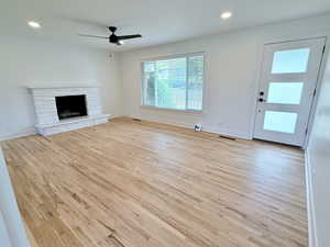Unfurnished living room featuring wood finished floors, ceiling fan, a stone fireplace, baseboards, and recessed lighting