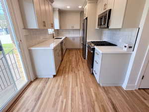 Kitchen featuring stainless steel appliances, a sink, light wood finished floors, decorative backsplash, and recessed lighting