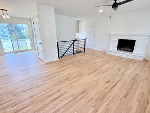 Unfurnished living room with wood finished floors, ceiling fan, baseboards, and a stone fireplace
