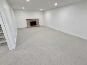 Unfurnished living room featuring recessed lighting, light colored carpet, baseboards, a stone fireplace, and stairs