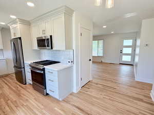 Kitchen with appliances with stainless steel finishes, light wood finished floors, light countertops, tasteful backsplash, and baseboards
