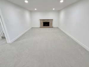 Unfurnished living room featuring recessed lighting, light colored carpet, baseboards, a stone fireplace, and stairs
