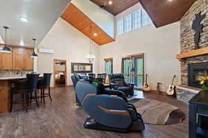 Living room featuring high vaulted ceiling, healthy amount of natural light, a chandelier, wood ceiling, and a stone fireplace