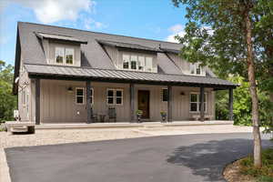 View of front facade with covered porch, a standing seam roof, board and batten siding, roof with shingles, and metal roof