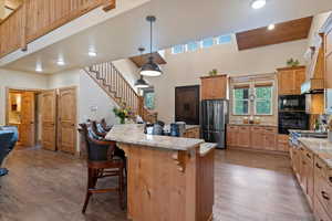 Kitchen with black appliances, a breakfast bar area, dark wood-type flooring, a center island, and light stone countertops