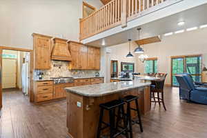 Kitchen with a towering ceiling, custom range hood, freestanding refrigerator, stainless steel gas cooktop, and dark wood finished floors