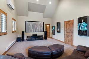 Cinema with a baseboard heating unit, a wall mounted air conditioner, carpet flooring, baseboards, and high vaulted ceiling