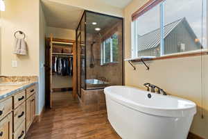 Bathroom with a stall shower, a freestanding bath, a spacious closet, vanity, and wood finished floors