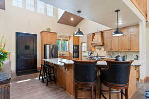 Kitchen featuring custom range hood, high vaulted ceiling, black appliances, decorative backsplash, and wood finished floors