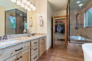Full bath featuring double vanity, a shower stall, a tub to relax in, wood finished floors, and a walk in closet