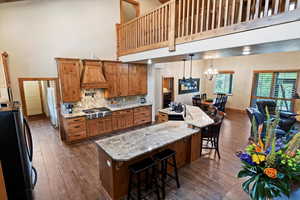 Kitchen featuring freestanding refrigerator, a towering ceiling, stainless steel gas stovetop, custom range hood, and brown cabinetry