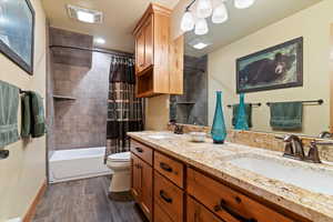 Bathroom featuring double vanity, shower / bath combo with shower curtain, toilet, wood finished floors, and baseboards