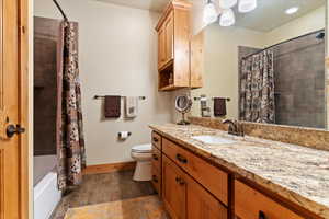 Bathroom featuring vanity, toilet, wood finished floors, shower / tub combo with curtain, and baseboards
