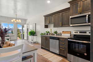 Kitchen with appliances with stainless steel finishes, dark brown cabinets, a chandelier, and recessed lighting