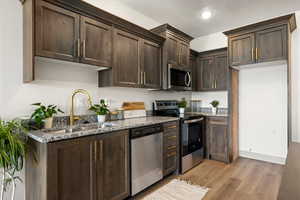 Kitchen featuring stainless steel appliances, dark brown cabinets, light wood-style floors, light stone counters, and recessed lighting