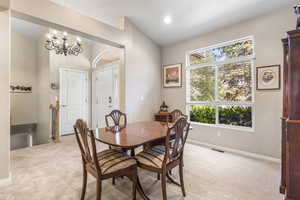 Dining area with lofted ceiling, light carpet, baseboards, and a chandelier