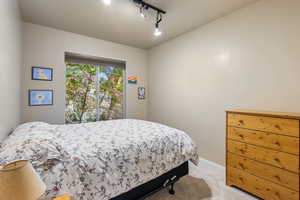 Bedroom with light colored carpet, rail lighting, and baseboards