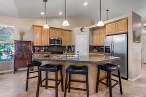 Kitchen with stainless steel appliances, a sink, decorative backsplash, lofted ceiling, and a breakfast bar
