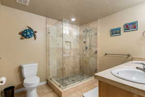 Full bath featuring toilet, a shower stall, a textured ceiling, vanity, and baseboards