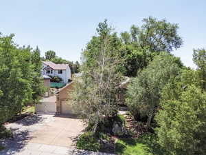 View of property hidden behind natural elements featuring driveway, stucco siding, a gate, and stone siding