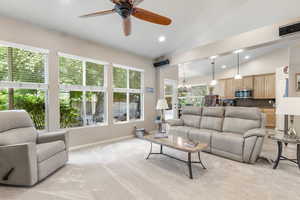 Living room featuring lofted ceiling, recessed lighting, a ceiling fan, a chandelier, and light carpet