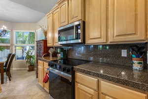 Kitchen featuring stainless steel microwave, tile counters, black electric range, tasteful backsplash, and baseboards