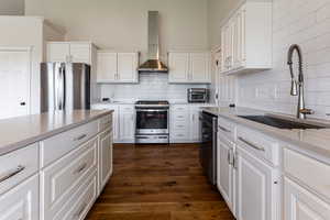Kitchen featuring quartz counter tops, stainless steel appliances, wall chimney exhaust hood, a sink, and white cabinetry.
