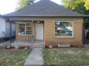 View of front facade with roof with shingles, a porch, brick siding, and a front lawn