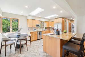 Kitchen with light brown cabinetry, white appliances, recessed lighting, a skylight, and a breakfast bar area