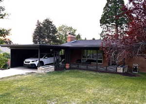 Ranch-style home featuring a carport, a chimney, a front lawn, and driveway