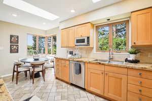 Kitchen featuring stainless steel dishwasher, a sink, white microwave, decorative backsplash, and light brown cabinets
