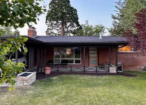 Back of property featuring a lawn, a chimney, brick siding, and a patio
