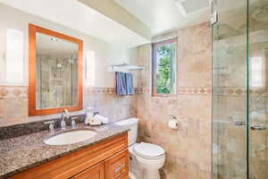 Bathroom with tile walls, vanity, a shower stall, and toilet
