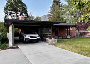 View of front of home with covered porch, a chimney, concrete driveway, an attached carport, and brick siding