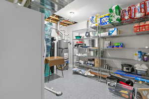 Basement utility room with additional storage space featuring oversized water softener, metal shelving and epoxy flooring