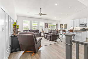 Living room featuring high vaulted ceiling with a recessed lighting and ceiling fan, decorative wainscoting wall trim, plantation shutters, light engineered hardwood flooring