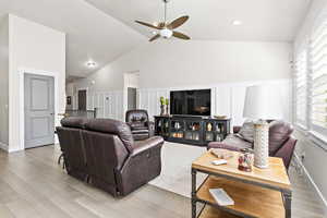 Living room featuring high vaulted ceiling with a recessed lighting and ceiling fan, decorative wainscoting wall trim, plantation shutters, light engineered hardwood flooring