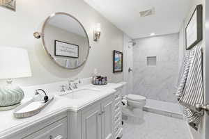Basement bathroom featuring toilet, vanity, floor to ceiling tiled shower, and recessed lighting