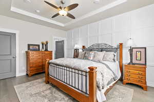 aster bedroom featuring coffered ceiling and ceiling fanlight, decorative wainscoting wall trim, and engineered hardwood flooring