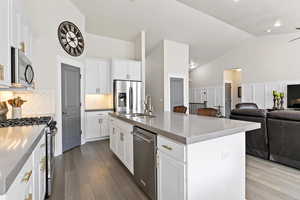 Kitchen with stainless steel appliances, decorative backsplash, under cabinet lighting, quartz counter-tops, island with additional cabinets, high vaulted ceiling, recessed lighting and light engineered hardwood flooring