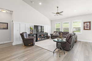 Living room featuring high vaulted ceiling with a recessed lighting and ceiling fan, decorative wainscoting wall trim, plantation shutters, light engineered hardwood flooring