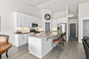 Kitchen with stainless steel appliances, decorative backsplash, under cabinet lighting, quartz counter-tops, island with additional  cabinets, high vaulted ceiling, recessed lighting and light engineered hardwood flooring