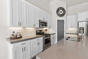 Kitchen with stainless steel appliances, decorative backsplash, under cabinet lighting, quartz counter-tops, island with additional cabinets, high vaulted ceiling, recessed lighting and light engineered hardwood flooring