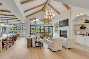 Living room featuring beam ceiling, light wood finished floors, a chandelier, a fireplace, and healthy amount of natural light